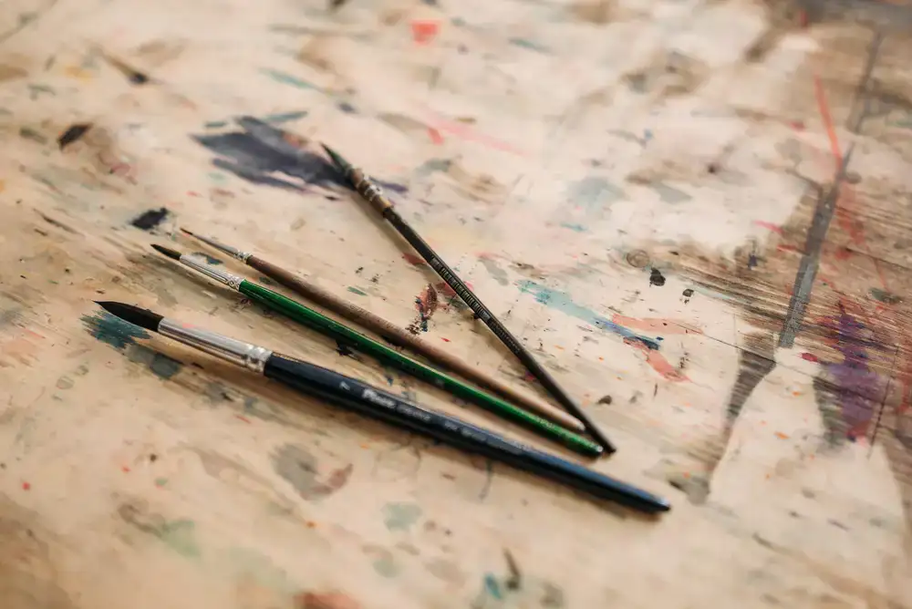 Sable brushes and enamel paints resting on a stained workbench
